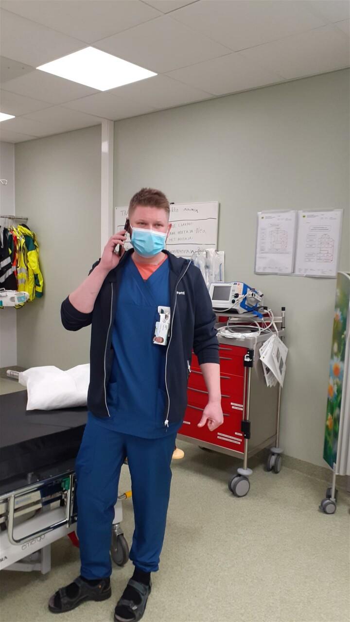 Henkilö soittaa puhelimella maski päässä sairaala alueella.
