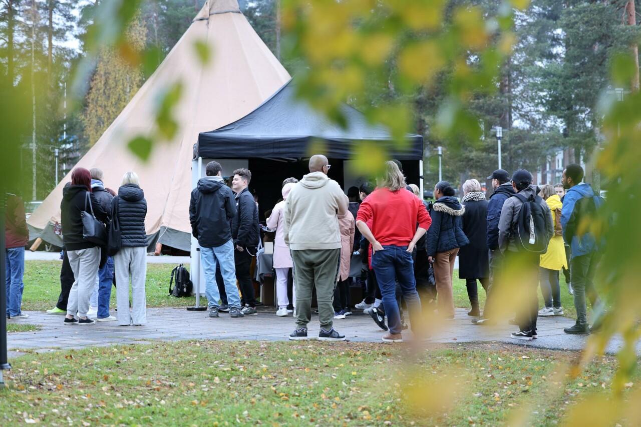 a group of people at an outdoor event, two tents can be seen in the background