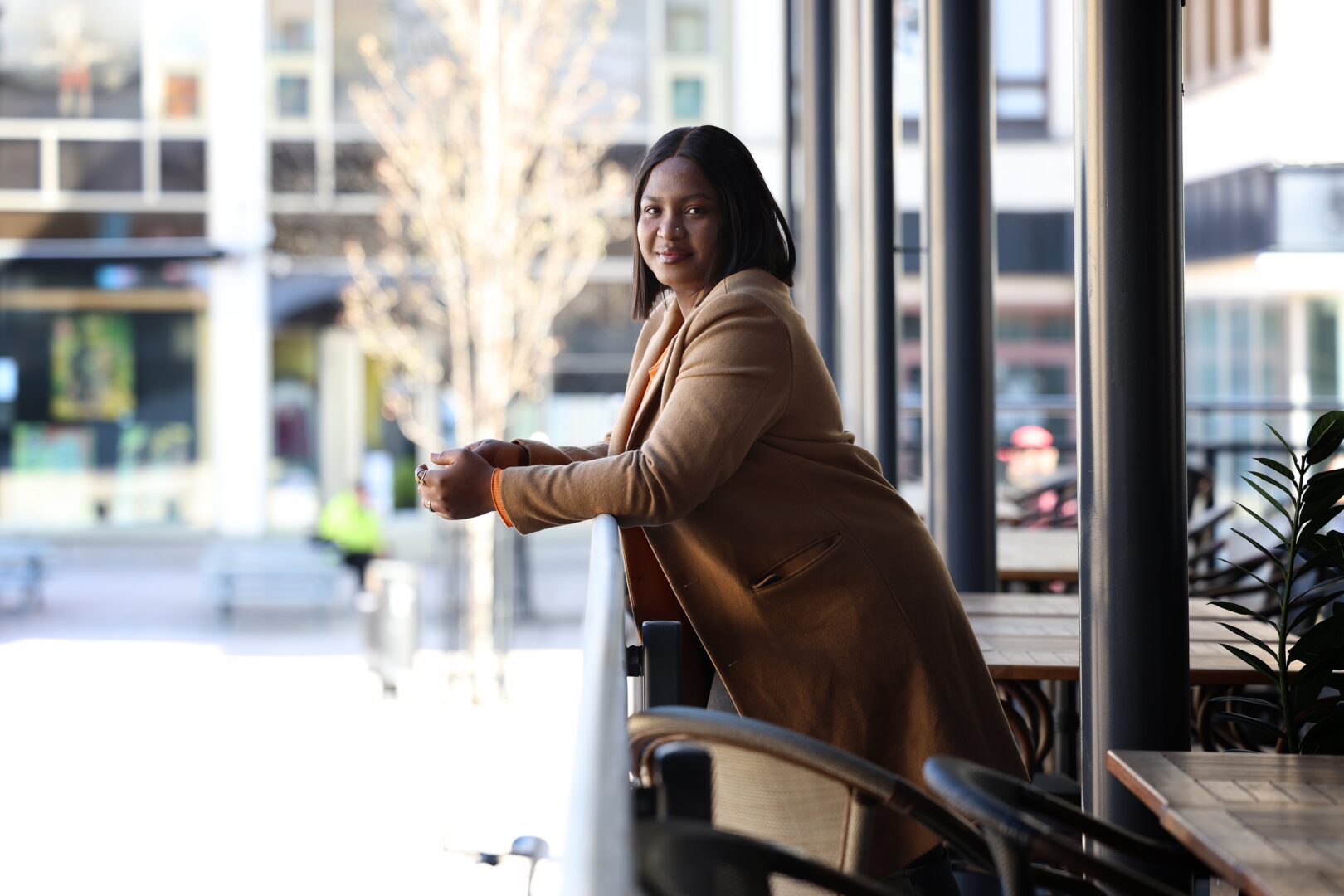 a woman in a brown coat leaning on the balcony railing.