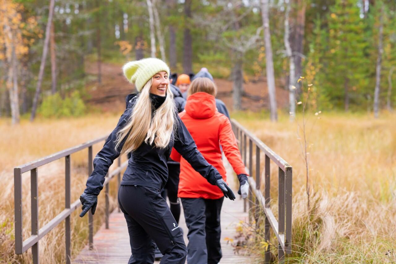 A group of young people are walking along the bridge, the back girl in the yellow cap has turned back and is smiling.