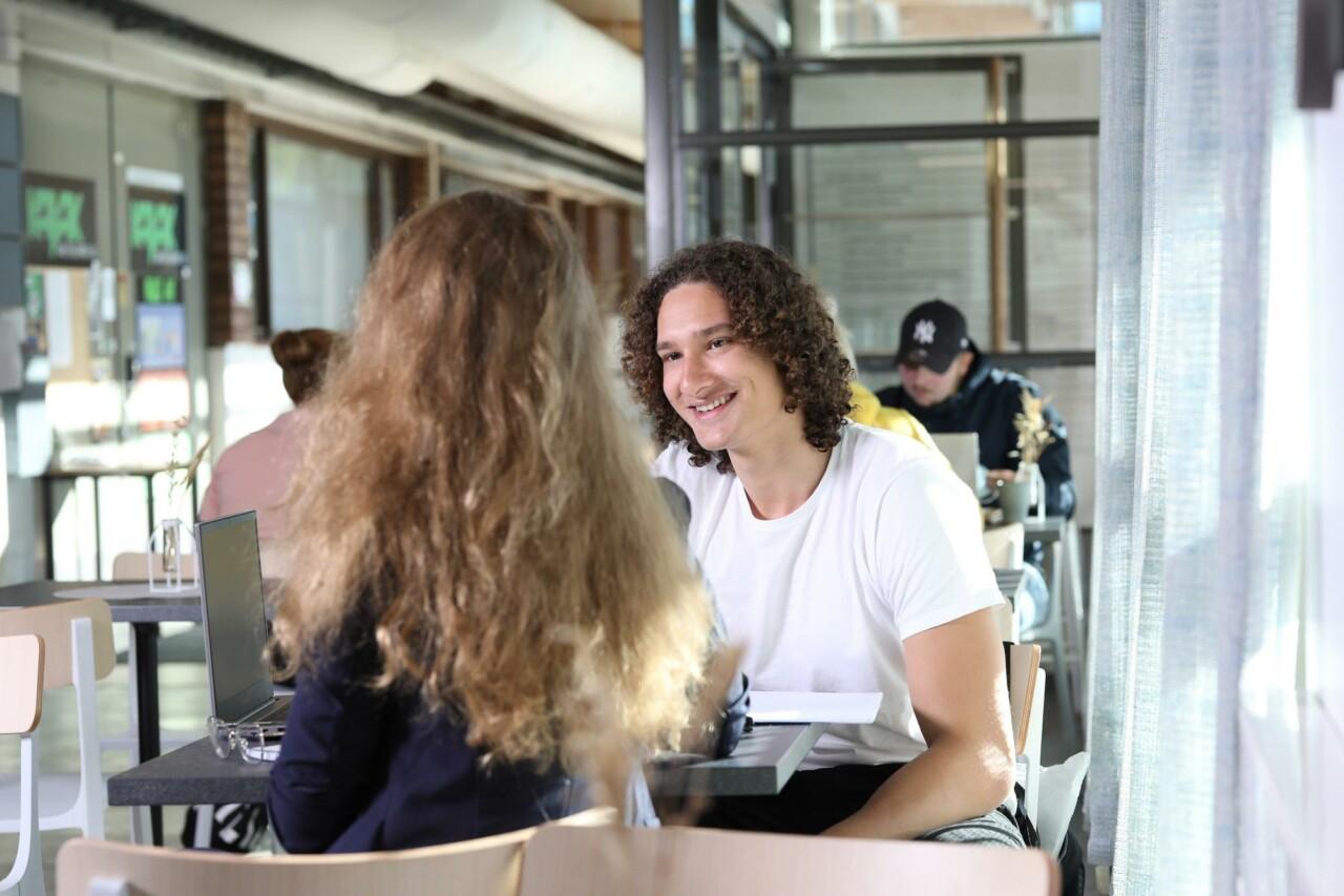 A boy and a girl sitting on their back are talking at a cafe table.