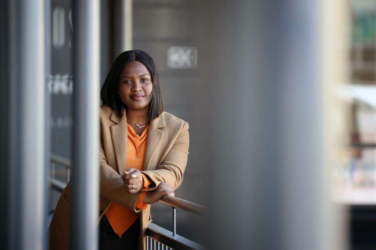 a woman in a brown coat leaning on a railing.