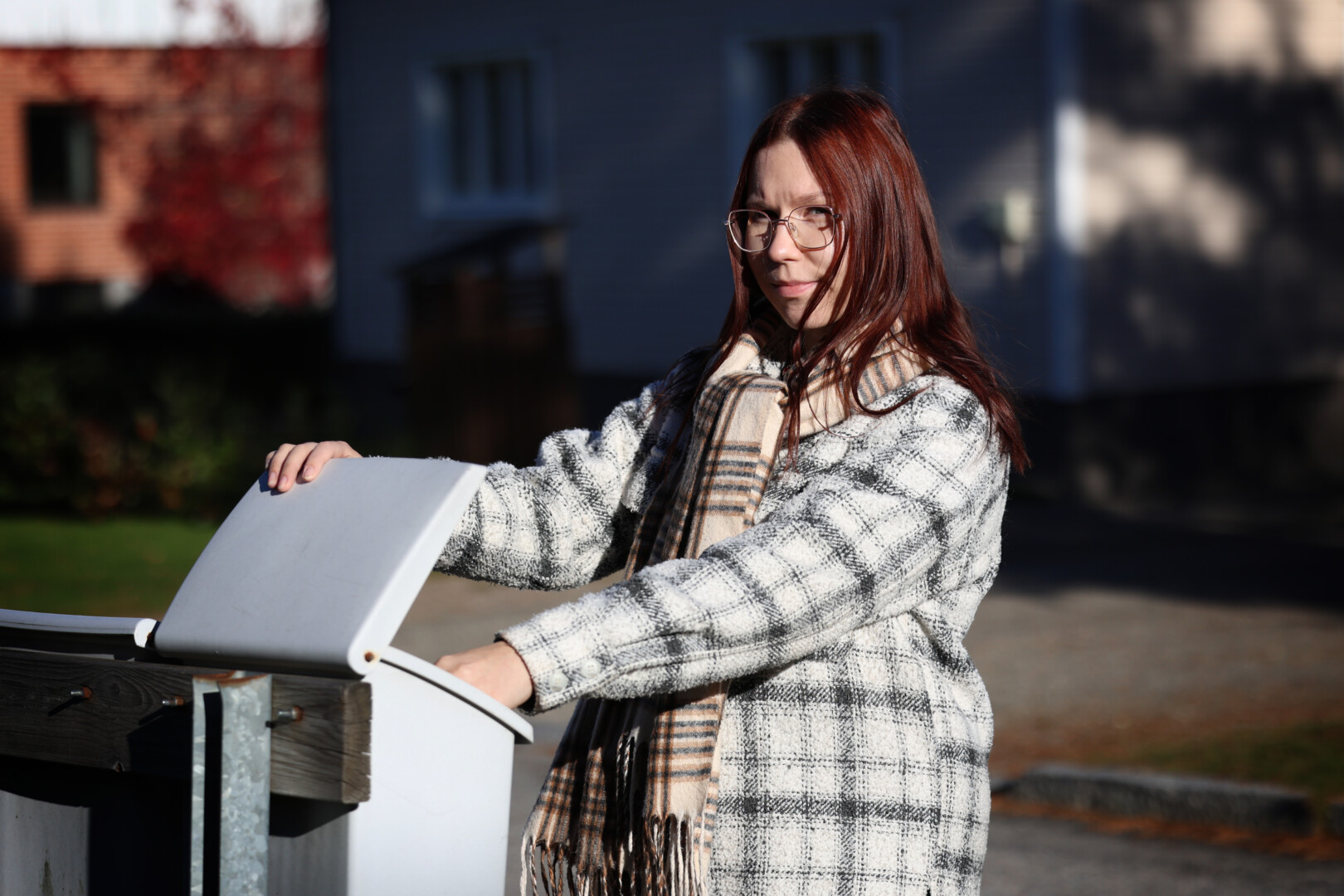 Ruskeahiuksinen nainen kurottamassa kädellään postilaatikkoon.