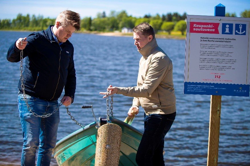 Kaksi miestä ovat rannassa soutuveneen ympärillä, pidellen ketjuja käsissään.