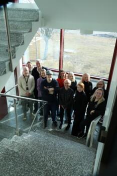The RDI personnel of Business at KAMK are standing on the landing in front of large windows. Photo: Kajaani University of Applied Sciences.