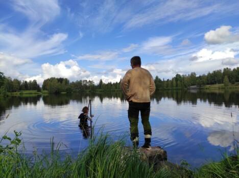 On a summer day a person is standing on rock by the lake, and another person is standing in a lake doing some research. Picture Ella Lukkari / KAMK.