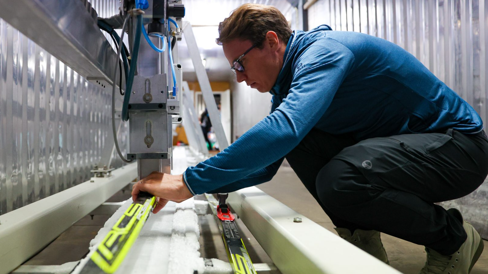 The person is placing skis into a testing device. They are wearing safety glasses and are in a crouching position. Photo: CEMIS.