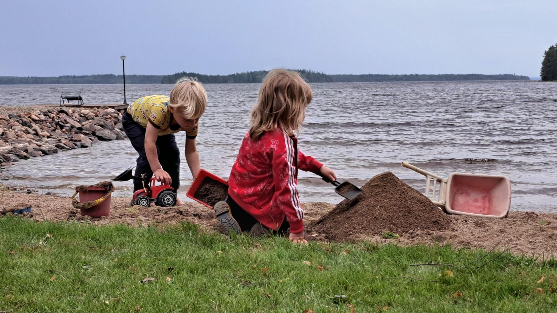 Two children are playing on a beach on a cloudy day. One child is playing with a toy tractor, while the other is building a sandcastle. Photo: Anne Kyllönen.